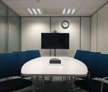 conference room with one white table with a tablet on it and a mounted tv on a wall across from the table