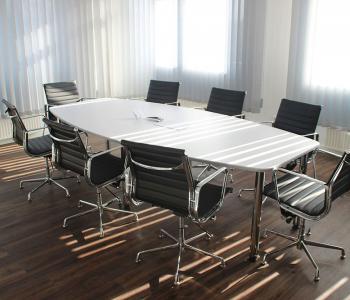 photo of a conference room. in it is a long white table that's empty, with 8 office chairs around it